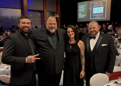 Group of four adults (three men in tuxedos, one woman in a black gown) smiling and posing together at their table during the WNY Heroes Red, White & Blue Charity Gala.