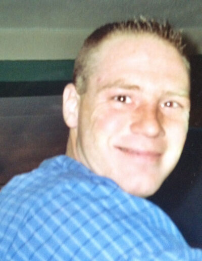 Young Heath McMillin in a blue plaid shirt, smiling brightly at the camera in a casual indoor setting.