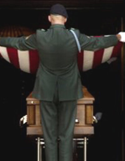 Honor guard soldier in dress uniform presenting the folded American flag during a military funeral service.