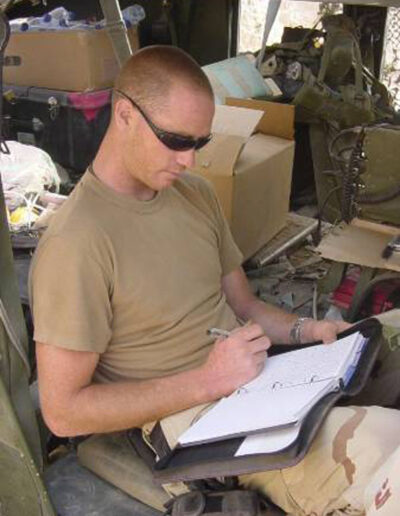 Heath writing in a notebook inside a military vehicle, surrounded by gear and supplies during his tour in Iraq.