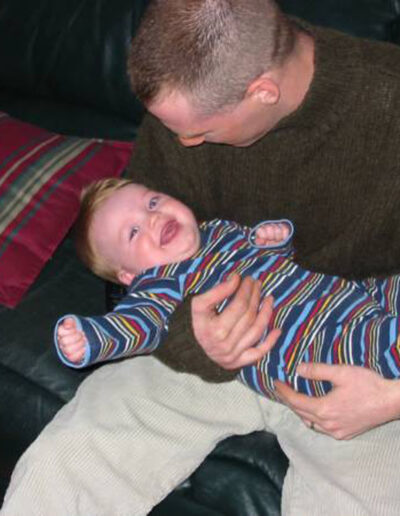 Heath grinning widely inside a military vehicle during deployment, dusty desert surroundings visible behind him.