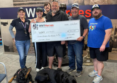 Five people and two relaxed service dogs in vests pose with an oversized ceremonial check for $750,000 made out to WNYHeroes for the Pawsitive for Heroes program.