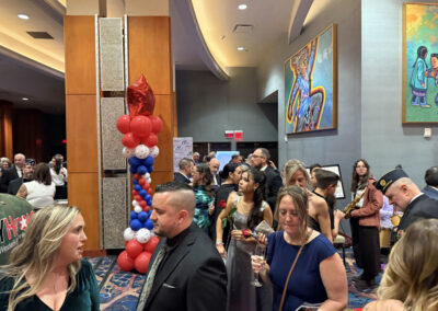 Pre- or post-dinner mingling area with attendees holding drinks, red-white-blue balloon column, and a banner reading “Red, White & Blue Charity Gala – WNYHeroes proudly presented by the New Era Cap Foundation.”