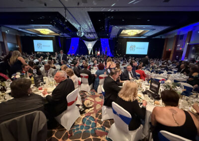 Another wide view of the packed ballroom at the WNY Heroes gala with blue lighting, disco ball reflections, red-white-blue chair sashes, and the WNYHeroes logo on big screens.