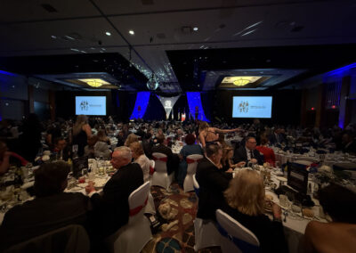 Wide shot of the ballroom at Seneca Niagara during the WNY Heroes Red, White & Blue Charity Gala, showing hundreds of formally dressed guests at round tables facing the stage with large screens and patriotic decorations.