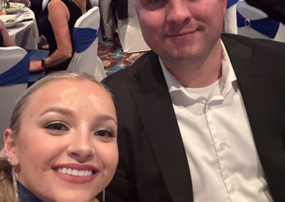 Young couple taking a selfie at their table during the WNY Heroes Red, White & Blue Charity Gala, both dressed formally, man making a peace sign behind the woman’s head.