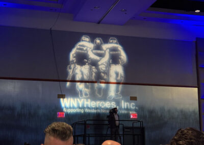 Projection on the wall showing three soldiers embracing with the text “WNYHeroes, Inc. Supporting Western New York Veterans” above seated gala attendees.