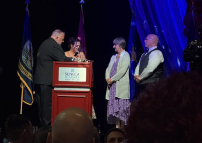 A man at the Seneca Niagara podium presents an award to a tearful woman in a sparkly dress, with two others standing nearby during the gala ceremony.