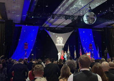 Large audience watching a stage presentation at the WNYHeroes gala under blue lighting and a disco ball, with the organization logo projected overhead.
