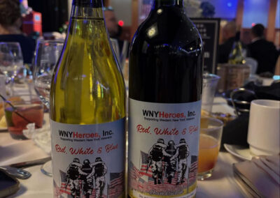 Two bottles of custom-labeled WNYHeroes “Red, White & Blue” wine (Chardonnay and Cabernet) on a banquet table at the charity gala.