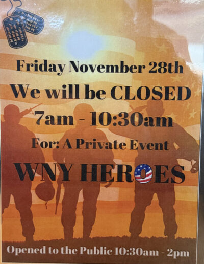 Sign on a diner wall announcing closure on Friday, November 28th from 7am–10:30am for a private WNY Heroes event, featuring silhouettes of soldiers and an American flag background.
